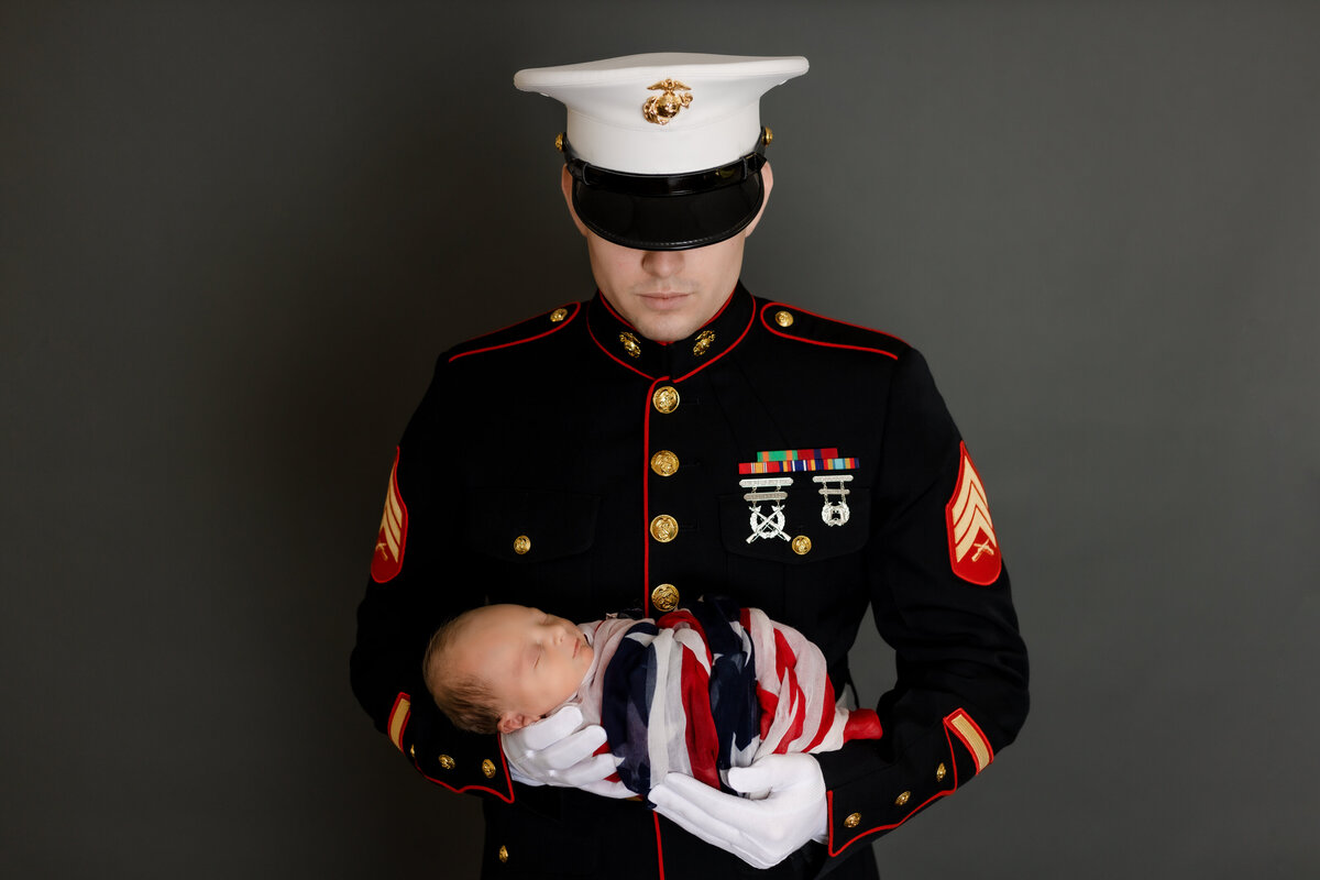 Newborn Photographer, a marine in dress blues holds his baby wrapped in an american flag