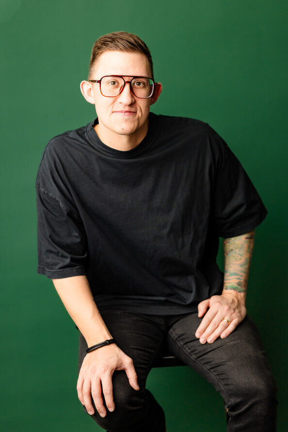 Man sits and puts hands on legs posing for his headshot.