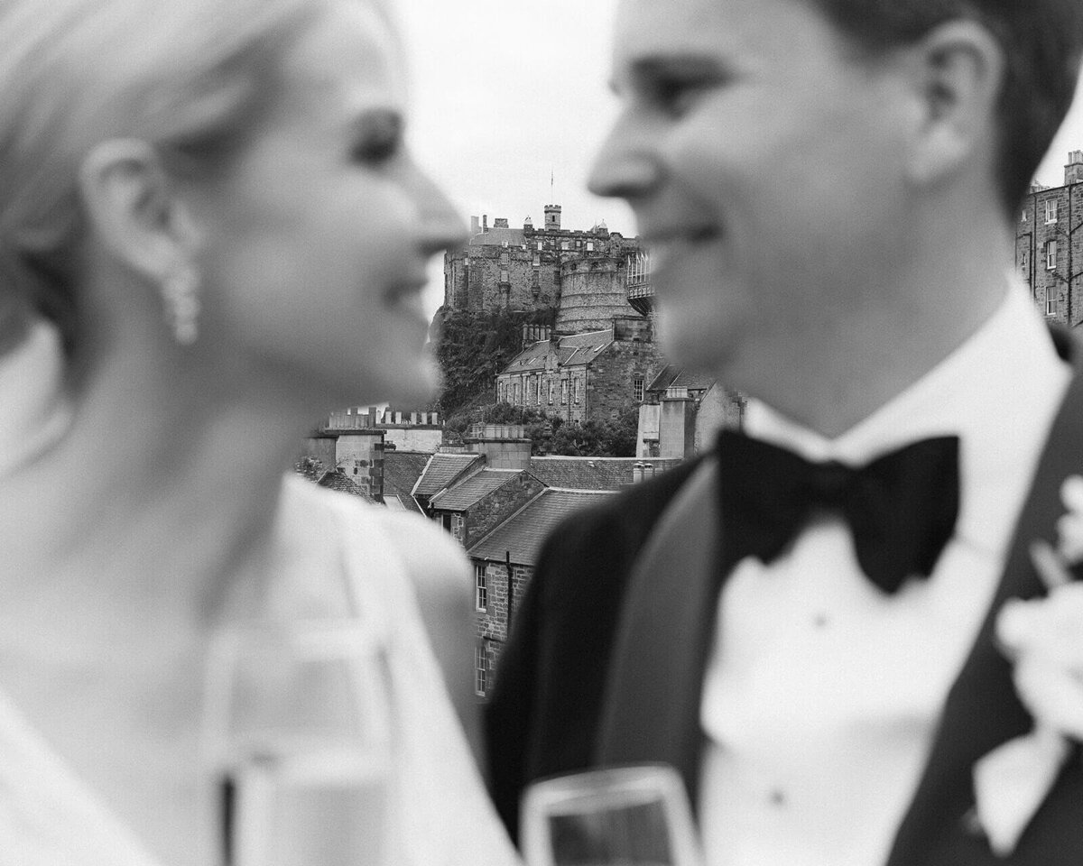 A couple out of focus stare at each other as the image focuses on Edinburgh castle behind them