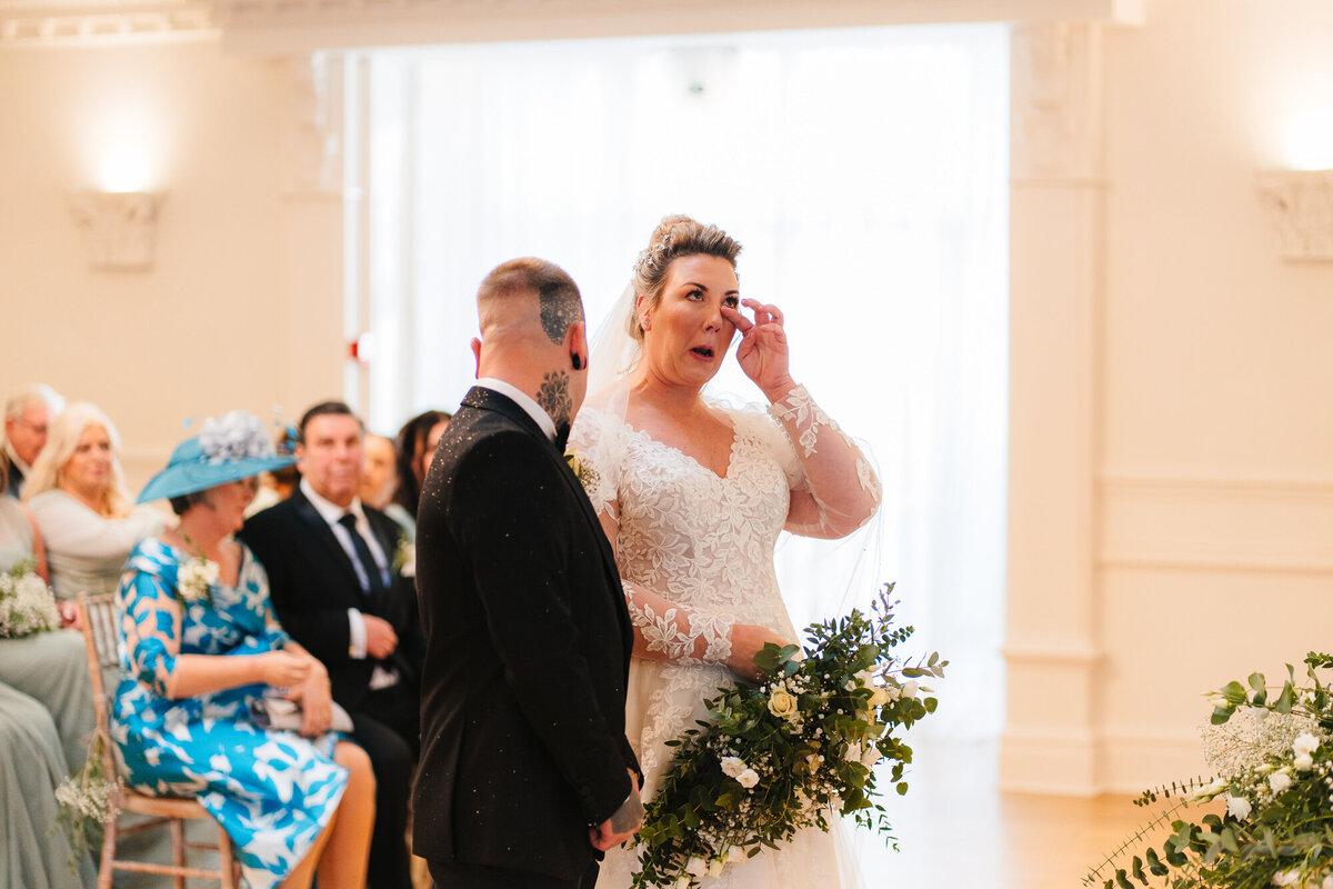 Bride wiping tears from her face  during the wedding ceremony at Ashfield House