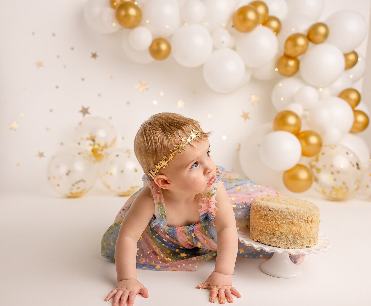 baby crawling around cake with gold balloons in the background