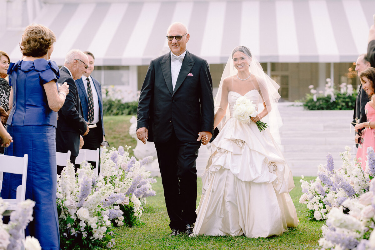 a bride and her father walk down the aisle during a wedding ceremony at Rosecliff Mansion