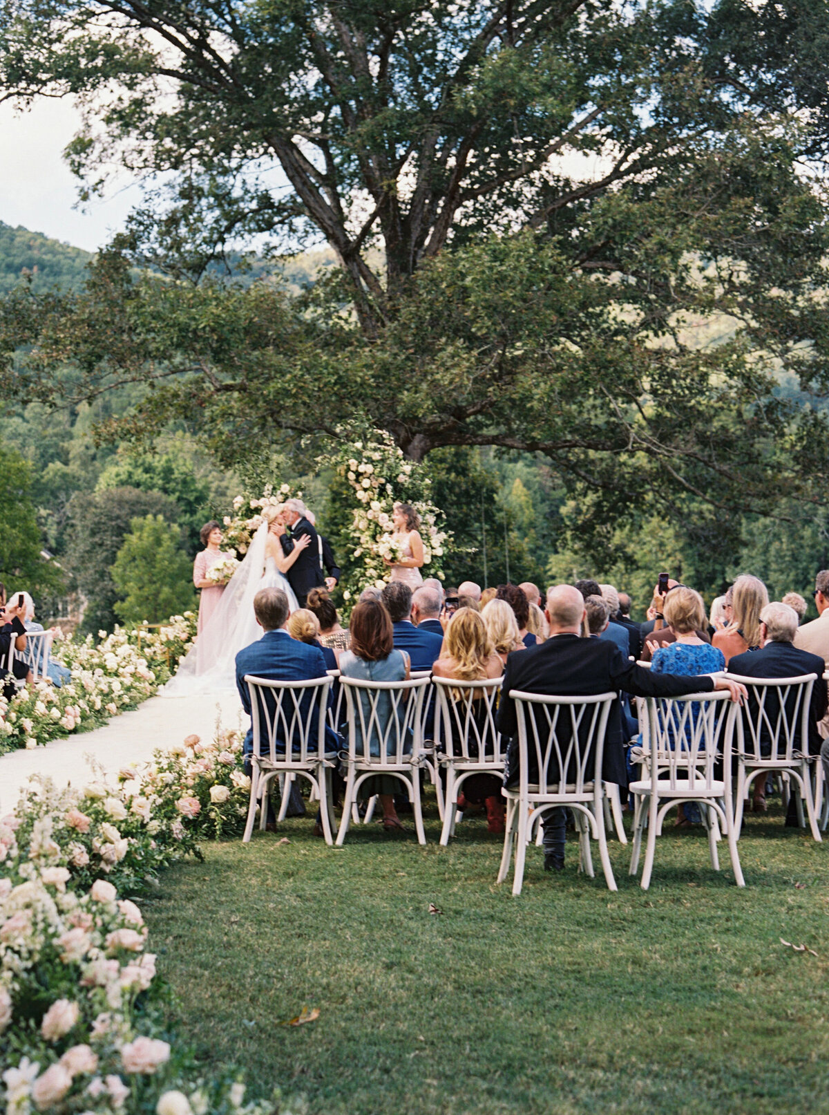 Epic ceremony backdrop for fall wedding at Blackberry Farms. Lush broken arch floral design for wedding ceremony backdrop. Garden inspired growing floral in colors of cream, white, blush, and green. Full coverage floral aisle for wedding ceremony. Floral meadows with petal heavy roses. Floral heavy flora design with elegant and whimsical design. Destination wedding at Blackberry Farm. Design by Rosemary & Finch Floral Design in Nashville, TN.