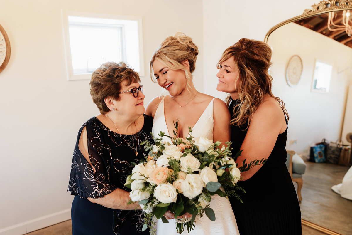 A bride and her mom smile at grandma on her wedding day.