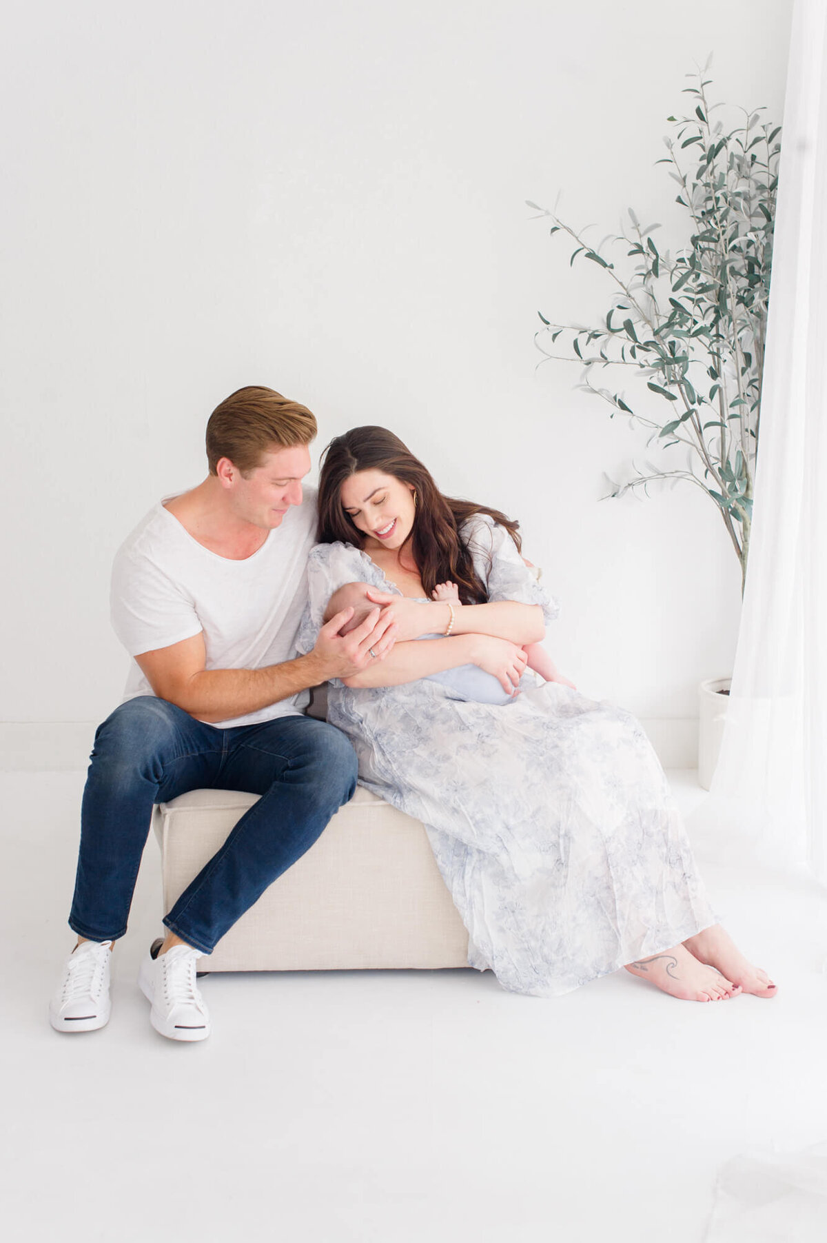 Beautiful natural light studio image of newborn parents holding the newborn boy on loveseat