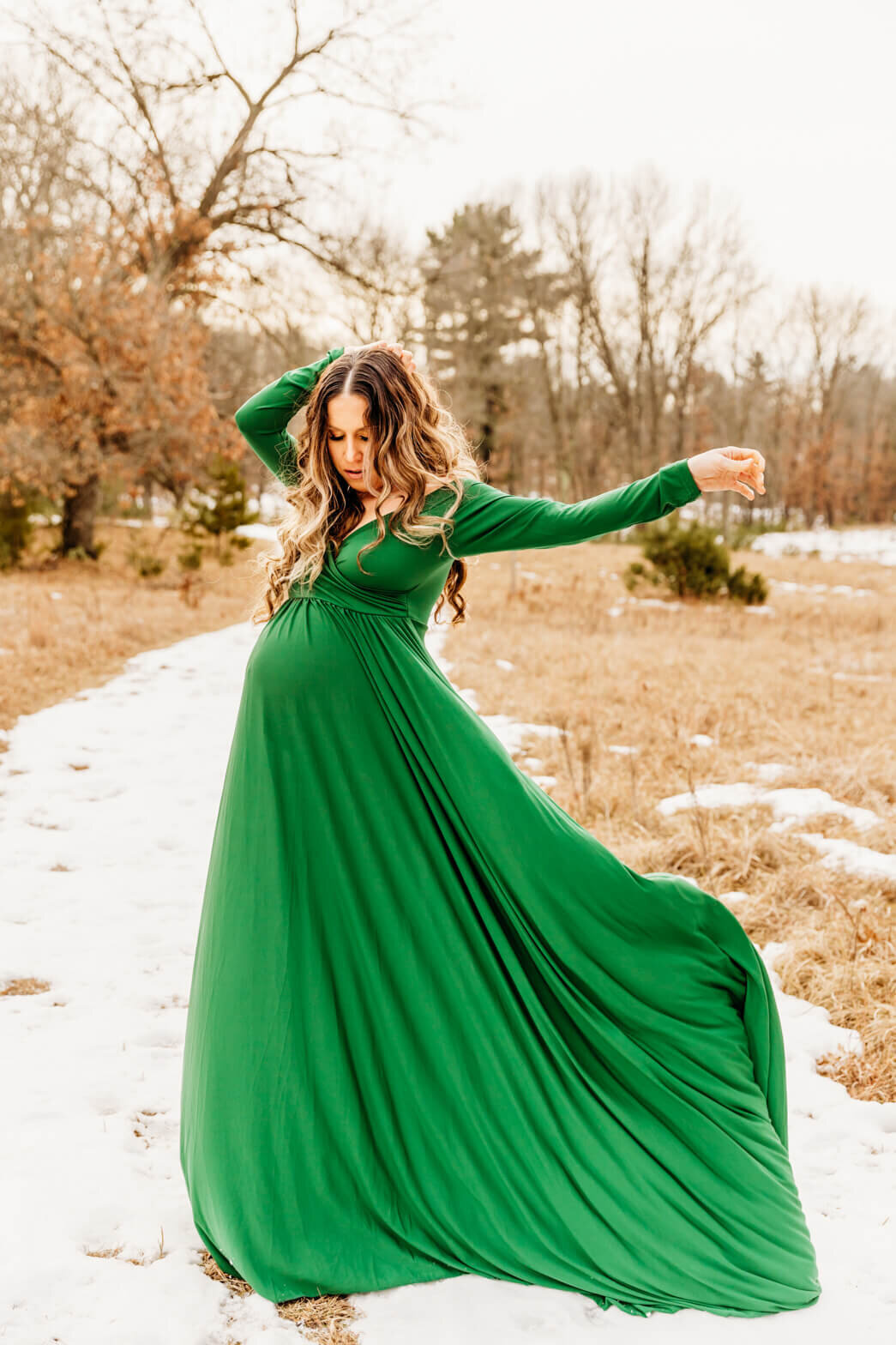 expecting mother throwing her green gown into the air during her winter maternity photo session.