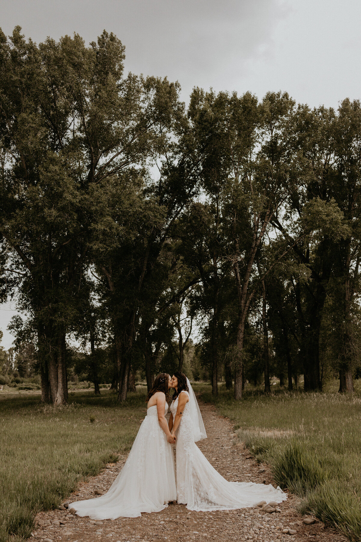 two brides kissing in front of tall green trees