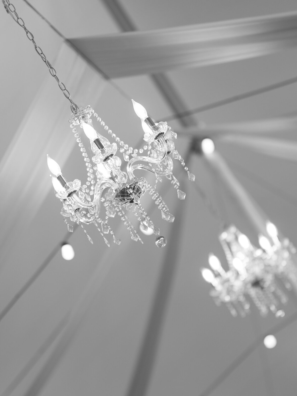 Crystal chandelier hanging in wedding tent with draped white fabric ceiling