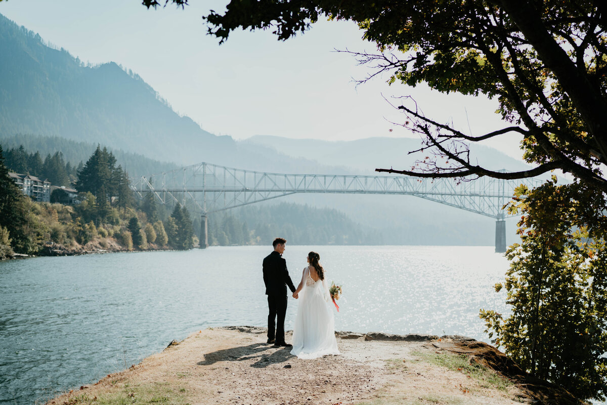 Bride and groom standing in front of the Columbia River Gorge with views of the Bridge of the Gods