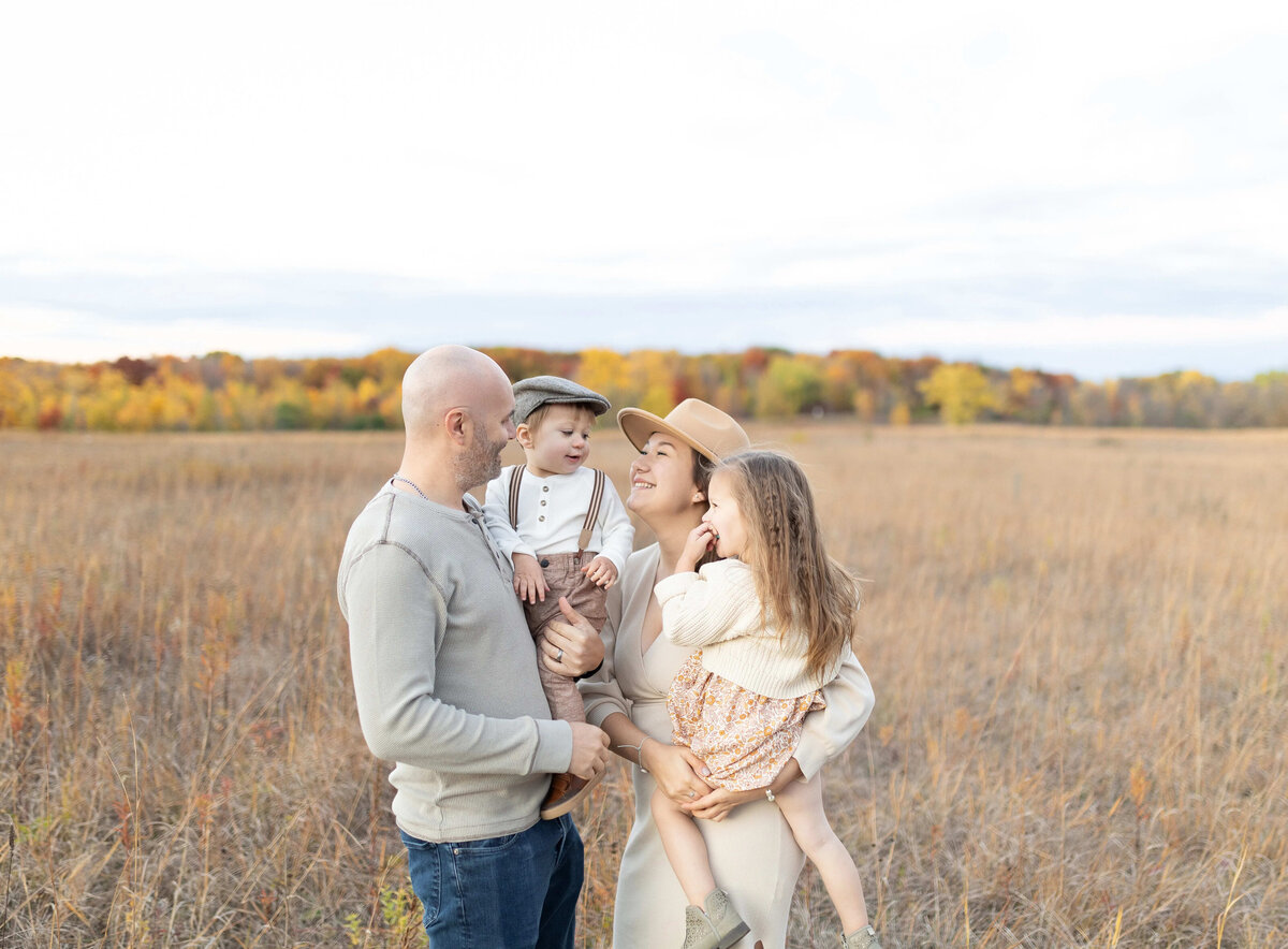 Mom and dad with two kids in golden field - candid family photo in Maple Grove at sunset
