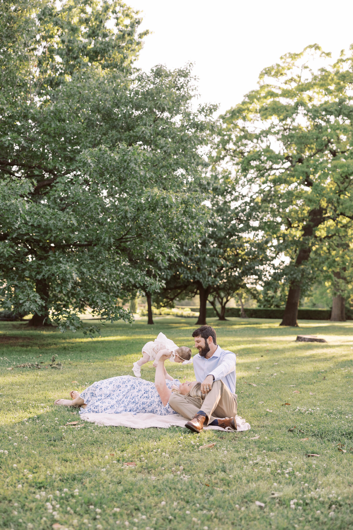young couple relaxes in grass while playing with 1 year old daughter during family phtoos