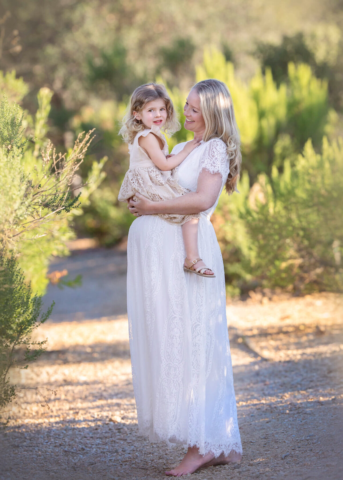 Mom to be with toddler daughter sitting on her baby bump at a Los Angeles park by Los Angeles Maternity Photographer