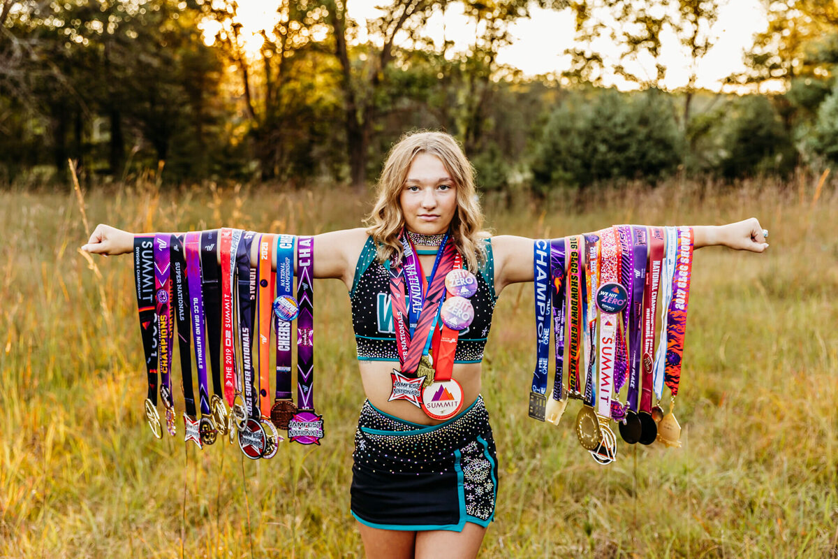 a champion cheerleader standing proud with her metals and she reaches her arms out to the side and her metals hanging down in a field near Oshkosh