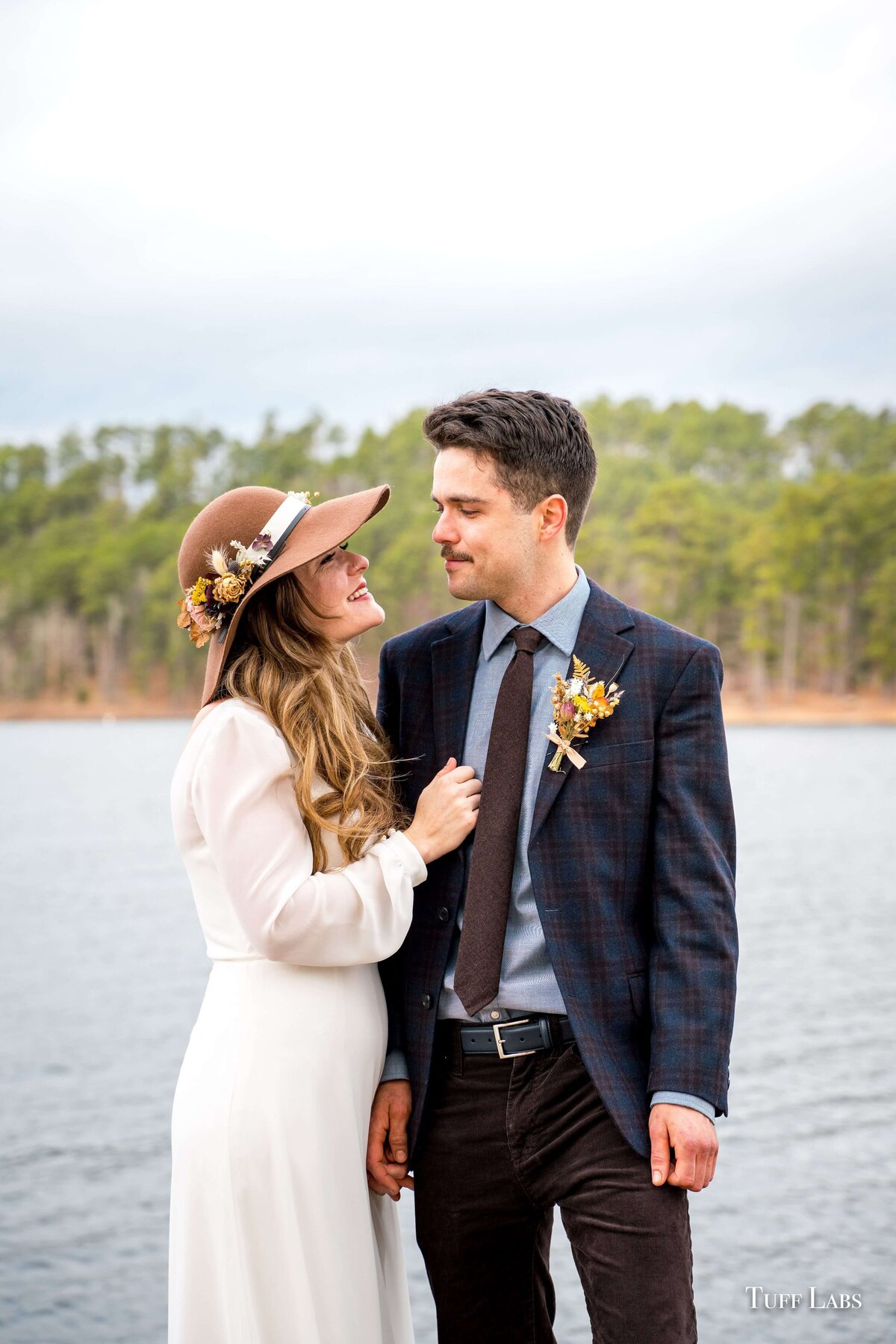A bride has dried flowers on her hat and looks at groom who has a dried flower boutonniere.