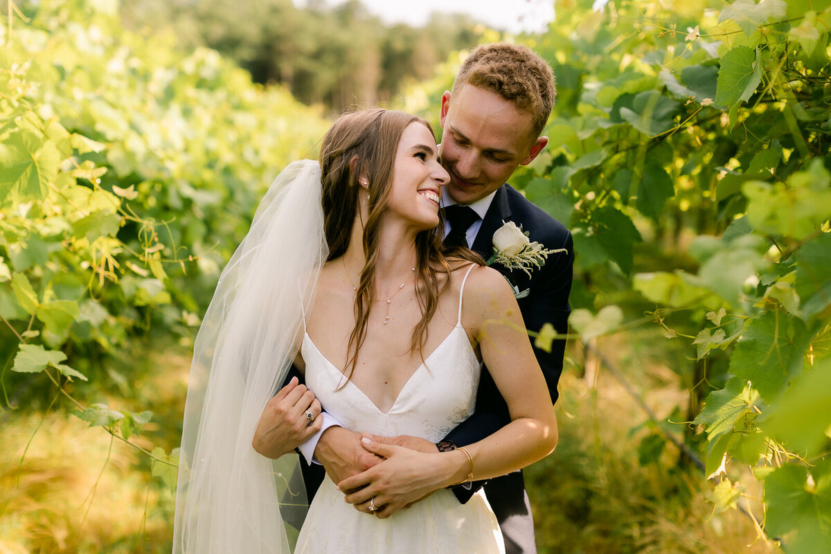 Wedding Photographer, a groom holds his bride from behind under the trees, they are smiling