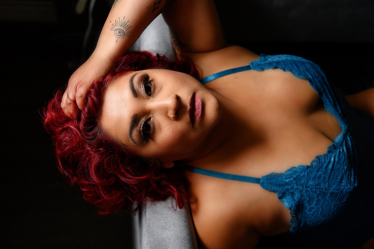 woman leaning back with red hair and a blue bodysuit with her hand in her hair for her Toronto boudoir photo session.