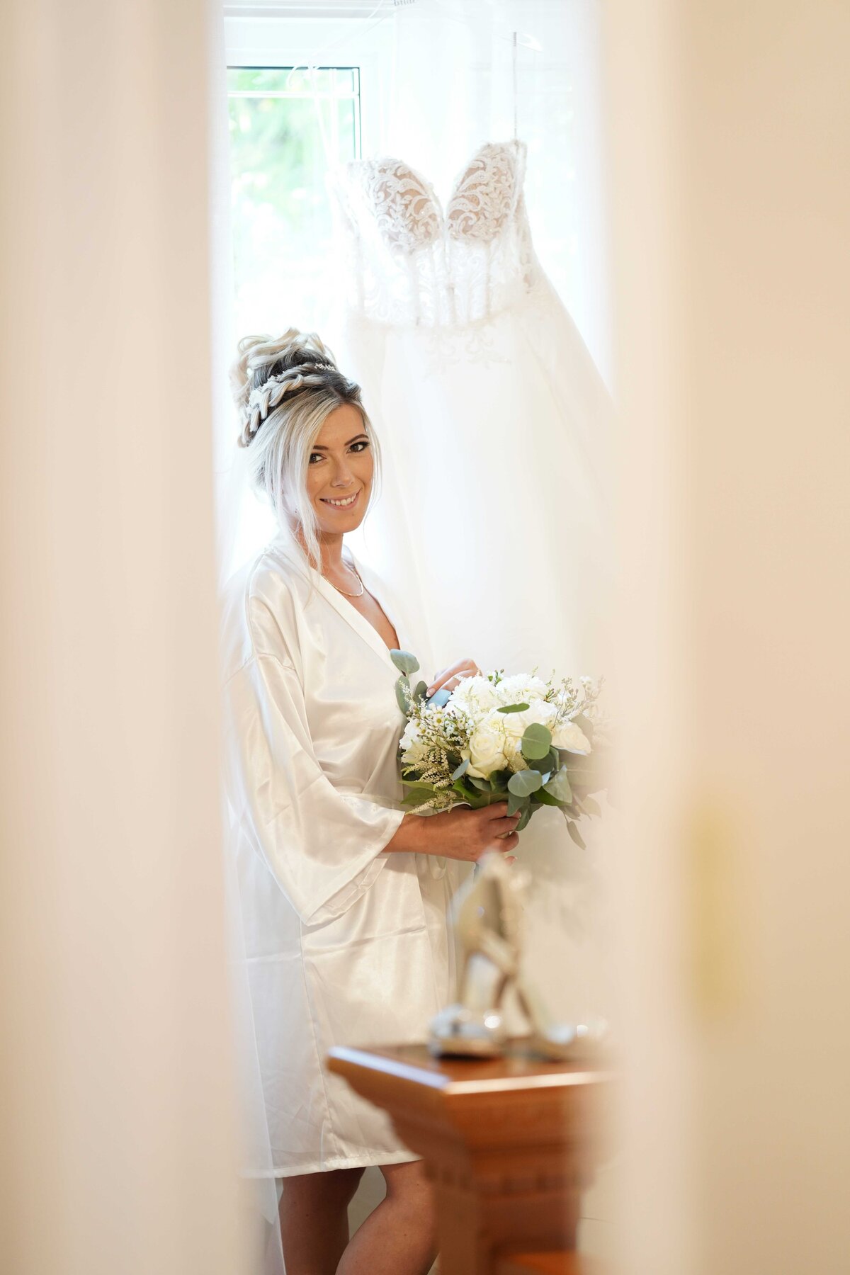 A bride is glimpsed through a doorway, adding a touch of intrigue and elegance to the bridal portrait. This image captures a candid and artistic moment, showcasing the bride’s grace and the atmospheric setting of her special day.