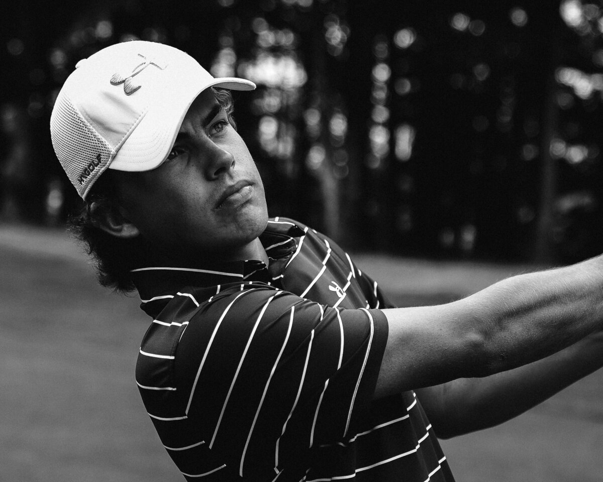 Closeup Black and white image of Garrett Risner after swinging golf club on fairway of hole 12 on a dark dreary day. Captured at The Club at 12 Oaks Holly Springs, NC in Spring 2020.