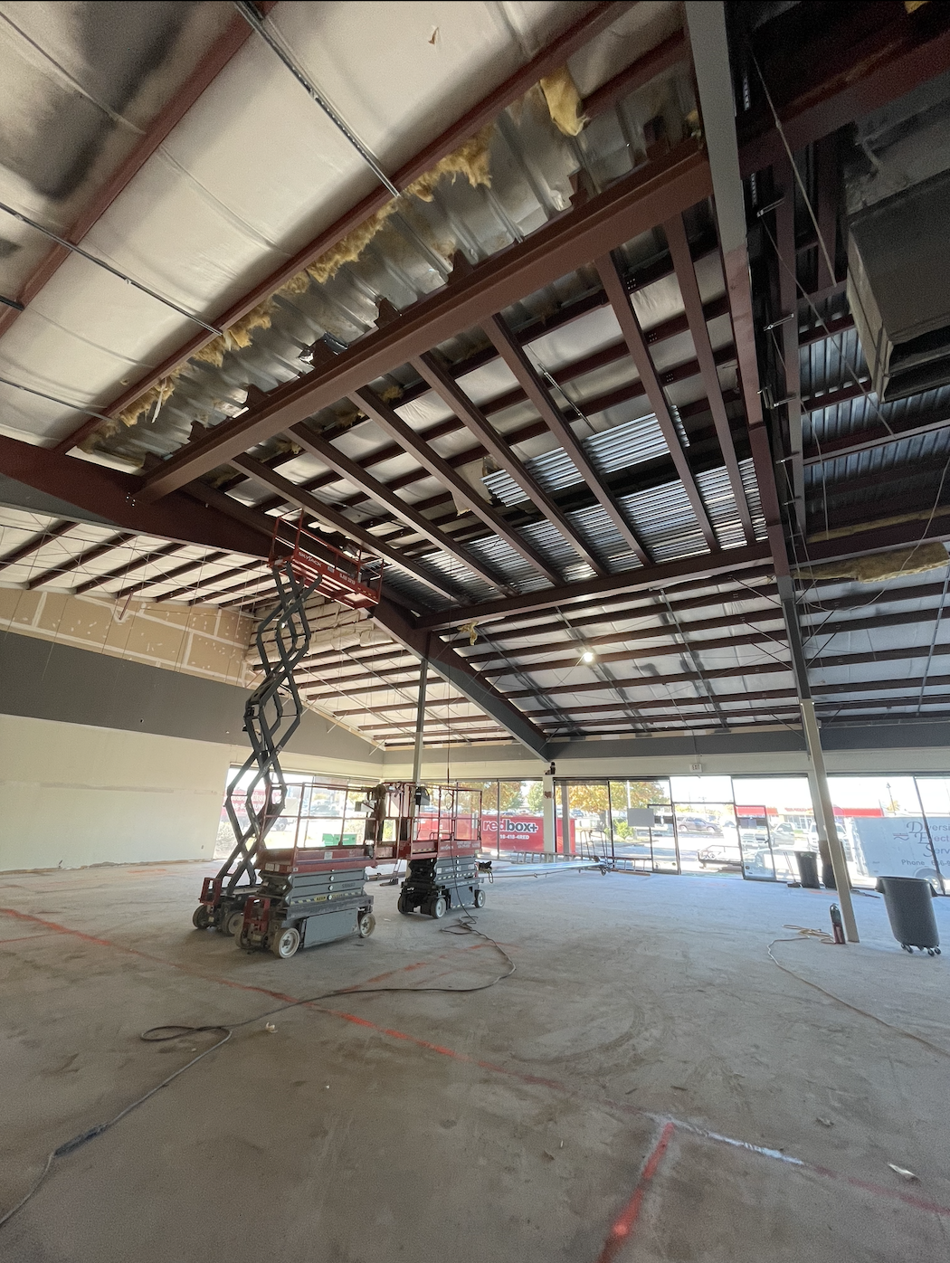 Interior view of structural steel roof framing and welded beam installation during commercial construction project.
