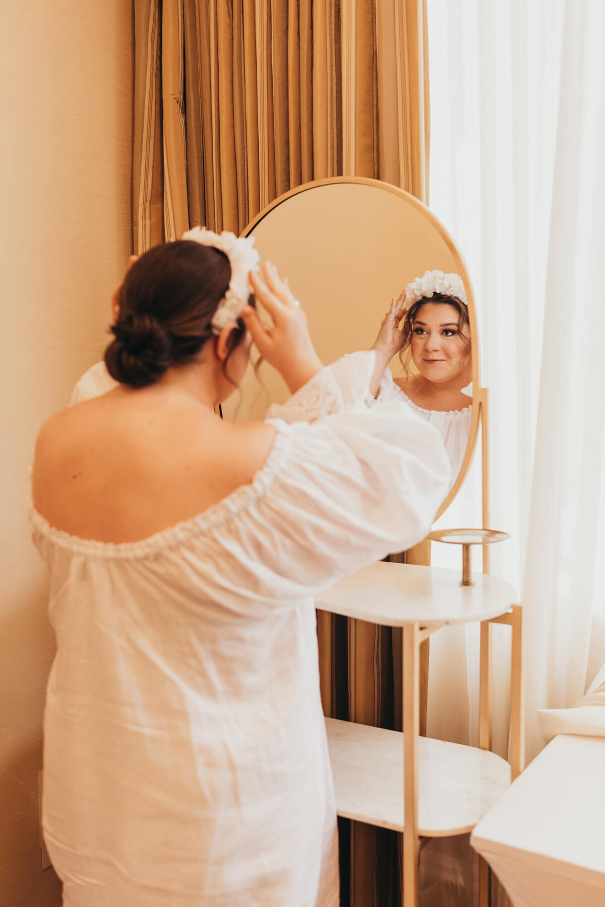 bride adjusts her floral tiara in the mirror