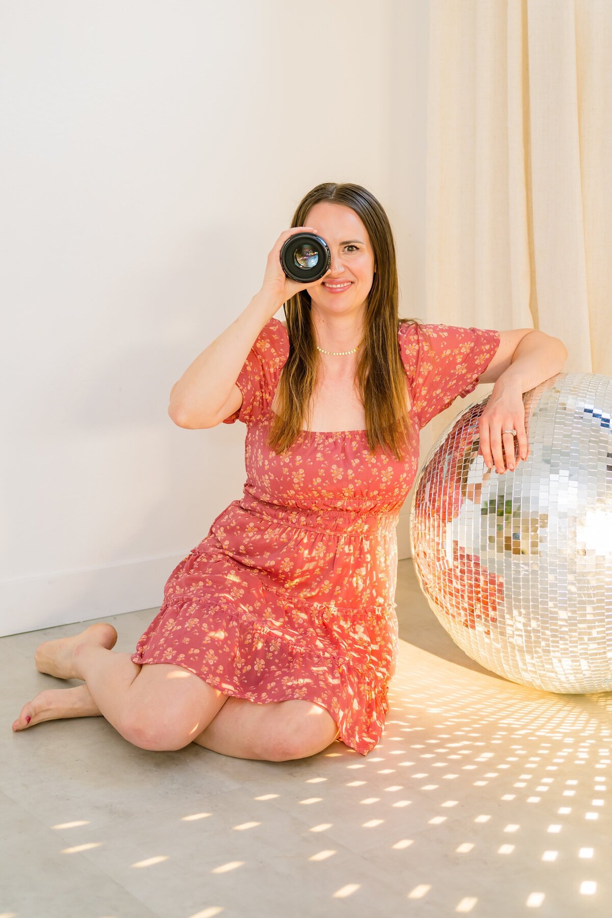 small business owner with a lense to her eye smiling at the camera