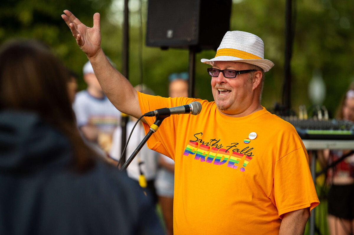 an event organizer in an orange t-shirt greeting attendees of the Tweed Canopy Growth Pride Parade.  Captured by Ottawa Event Photographer JEMMAN Photography COMMERCIAL 