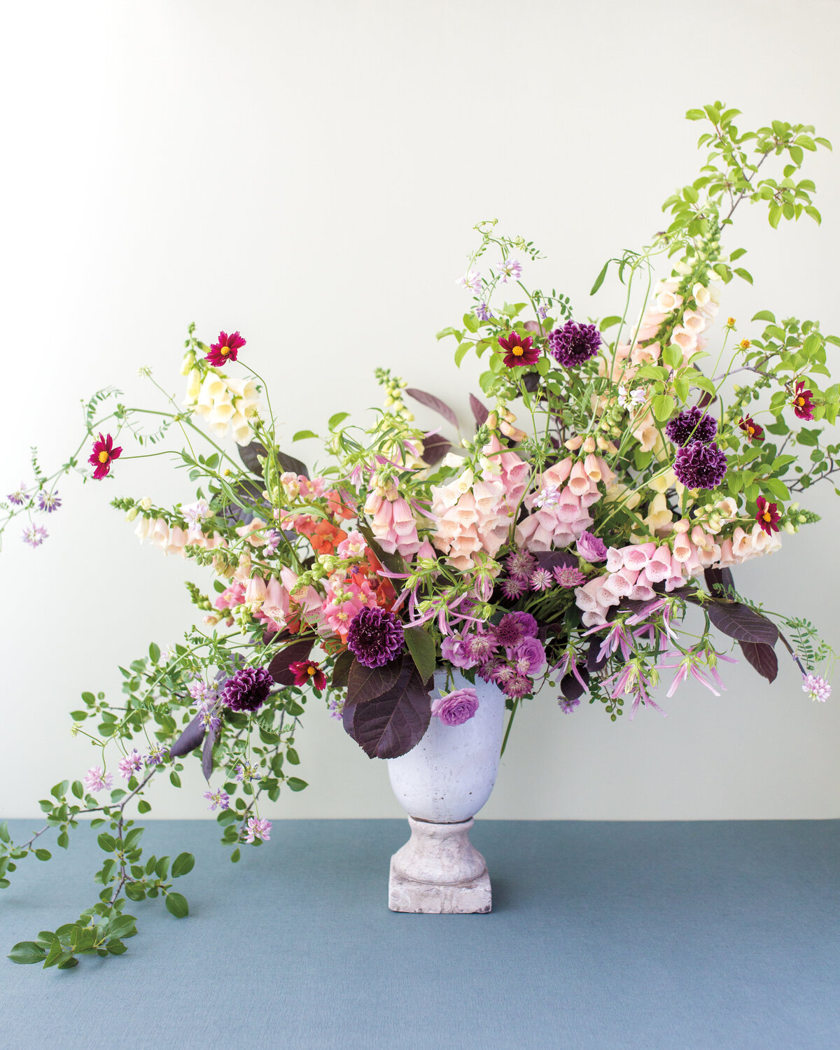 A cascading arrangement of bright pink and purple flowers sits in an urn on a blue floor.