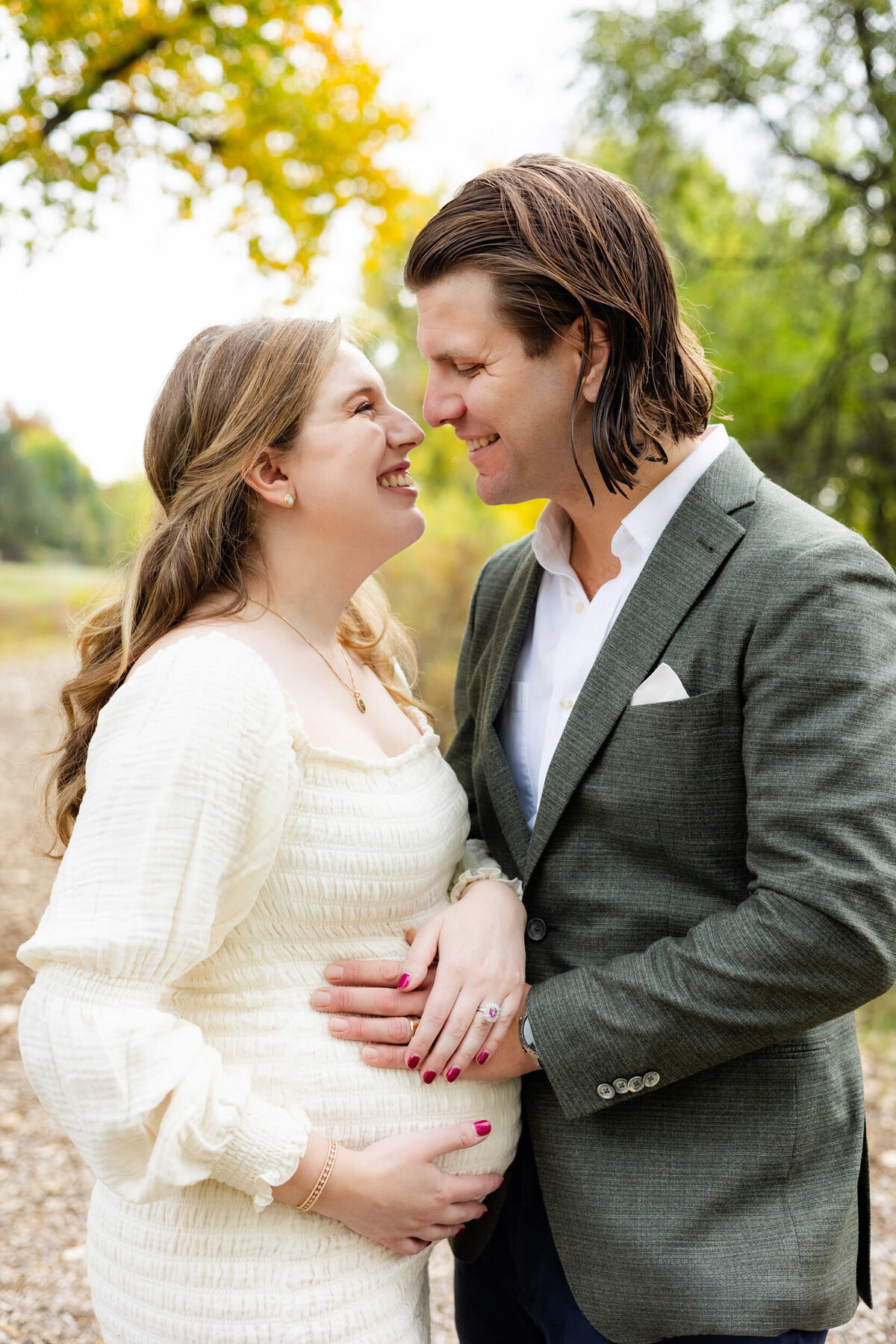 Husband and wife smile at each other while both have hands on wife's pregnant belly.