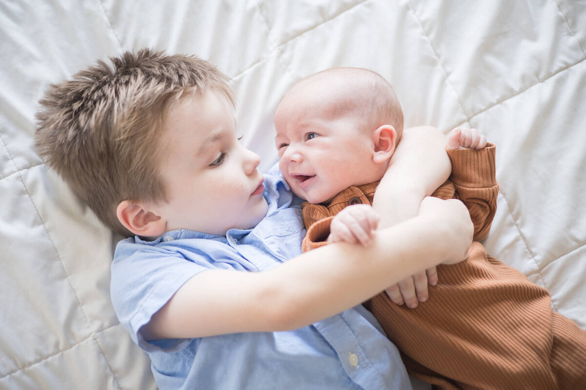 small boy cuddling with his newborn baby brother ina rust brown onesie