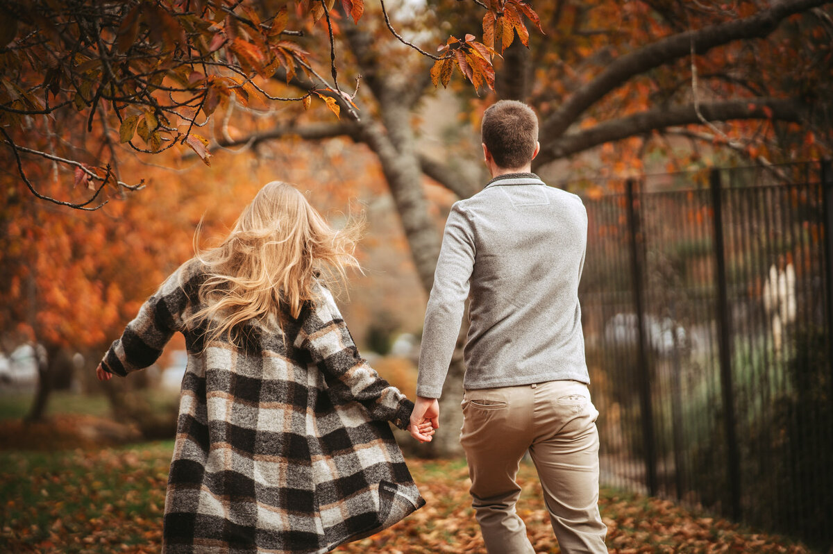 engaged couple running in leaves