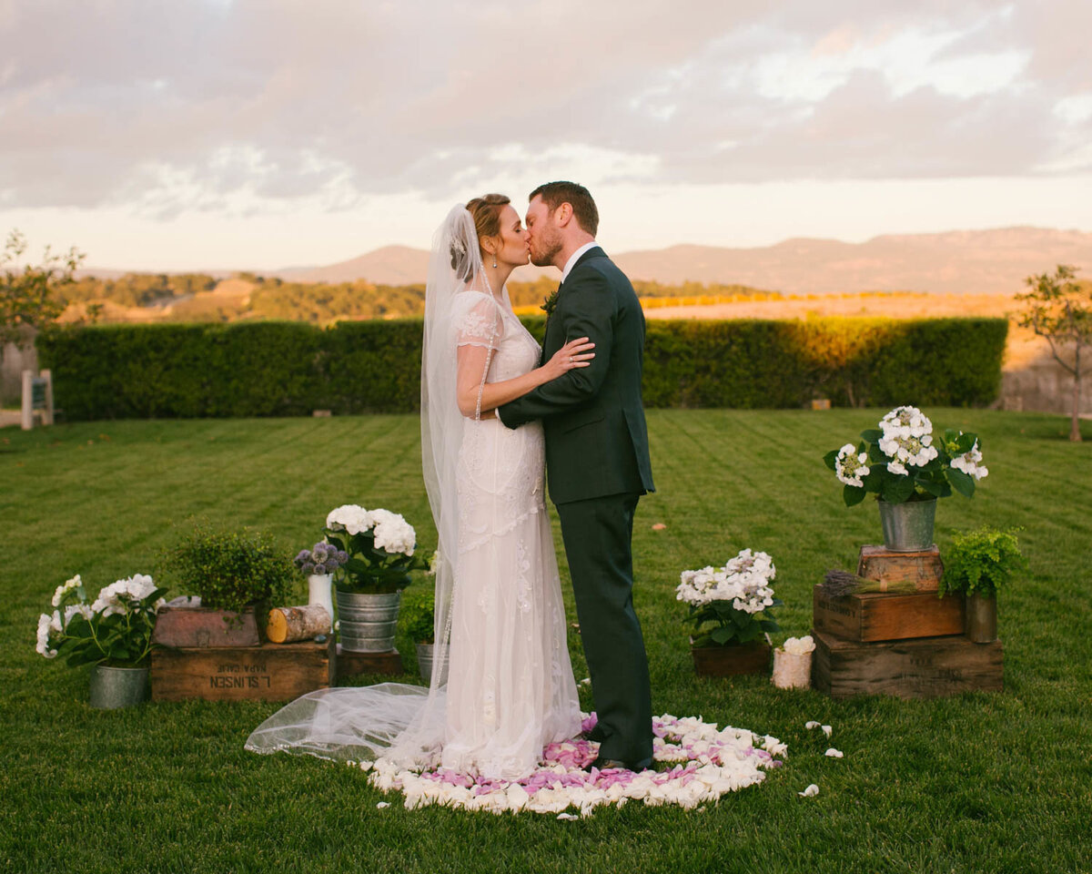 Couple stands on rose pedals sharing a kiss