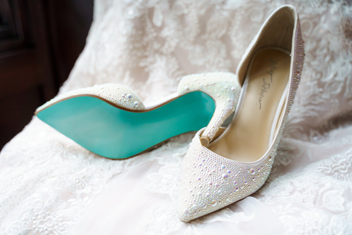 White beaded shoes with a teal bottom resting on a wedding gown at a wedding at the Wigwam Event Center in Pickerington, Ohio.