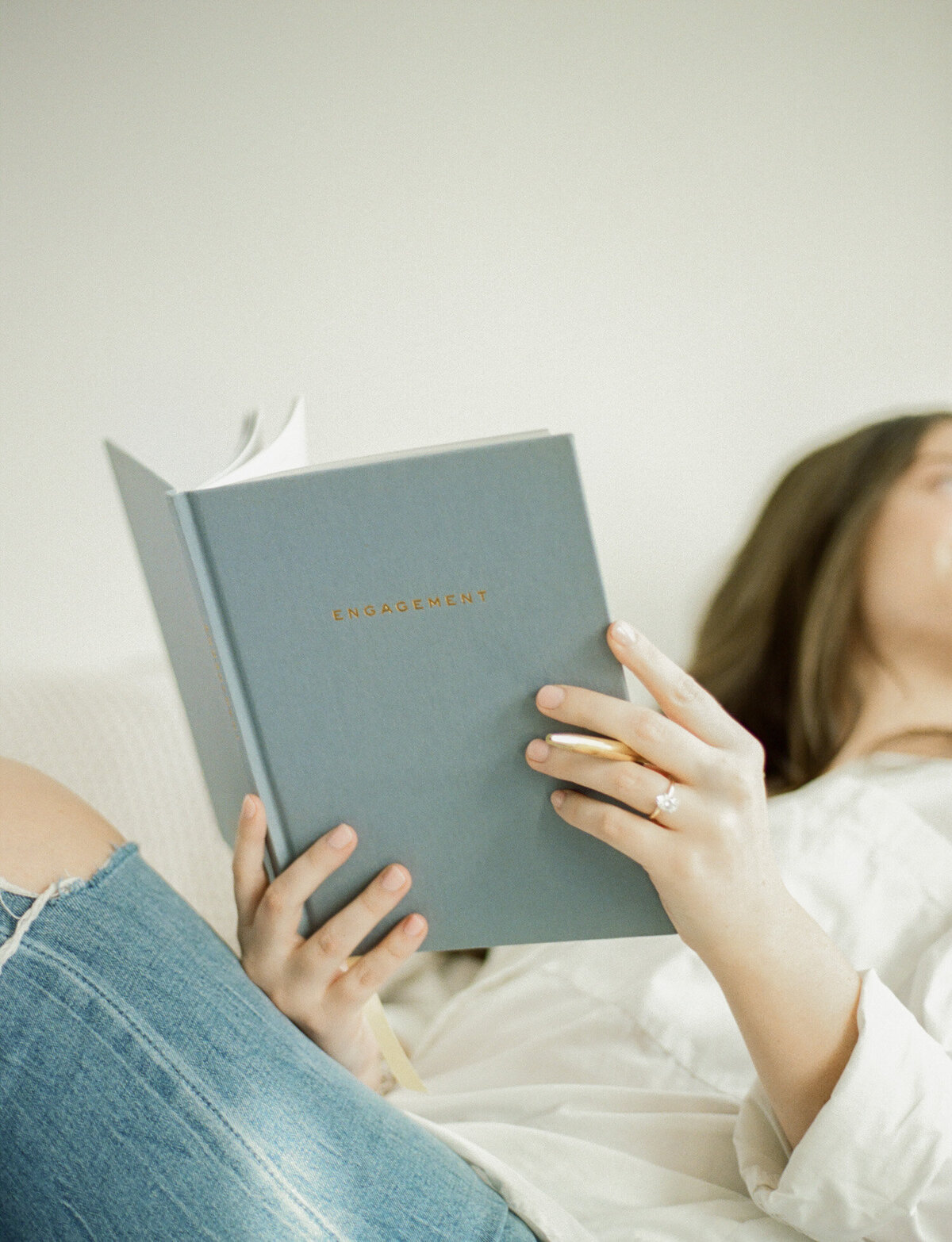 woman with ripped jeans holds light blue linen journal, Season Journals branding photography in white natural light studio
