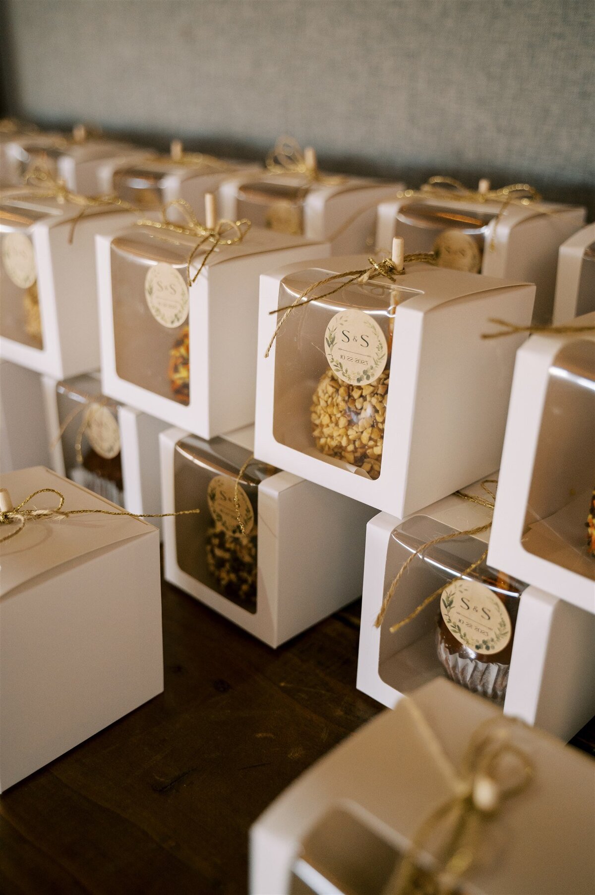 Elegant white gift boxes with clear windows displaying snacks, adorned with golden ribbons and tags by an Illinois wedding planner, arranged on a table.