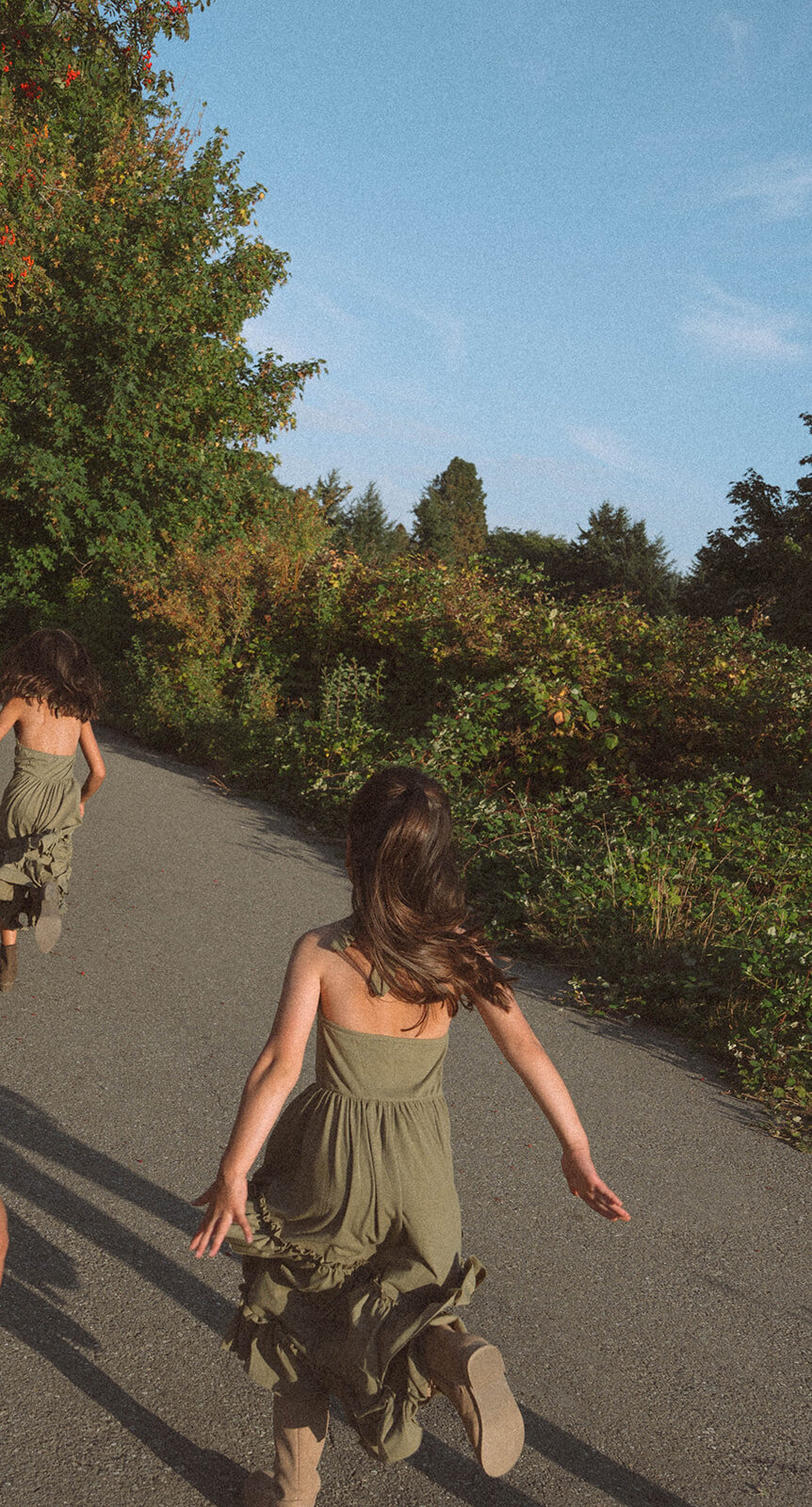 Two young girls running down a sunlit path in Irvine during candid family photos.