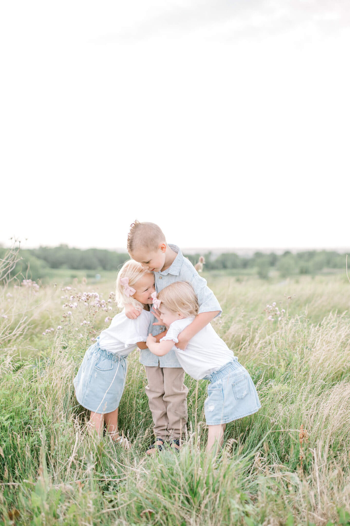 3 siblings hug eachother in a beautiful field of long grass