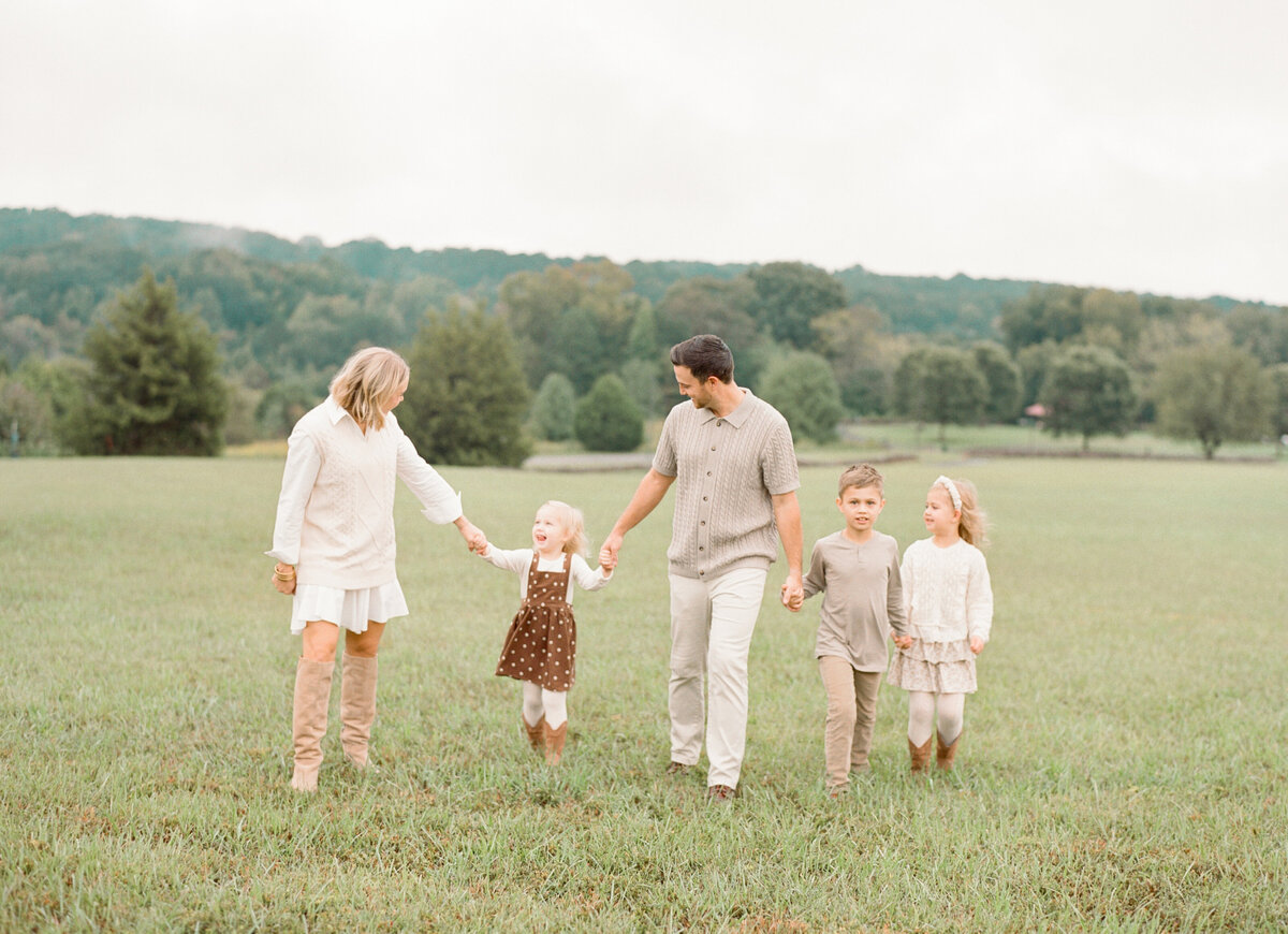 Family holds hands and walks through a field for their family session in Raleigh NC. Image by Raleigh maternity photographer A.J. Dunlap Photography.