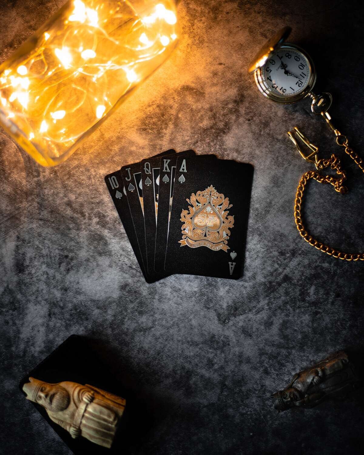 Black playing Cards, next to chess piece, fairy lights and pocket watch