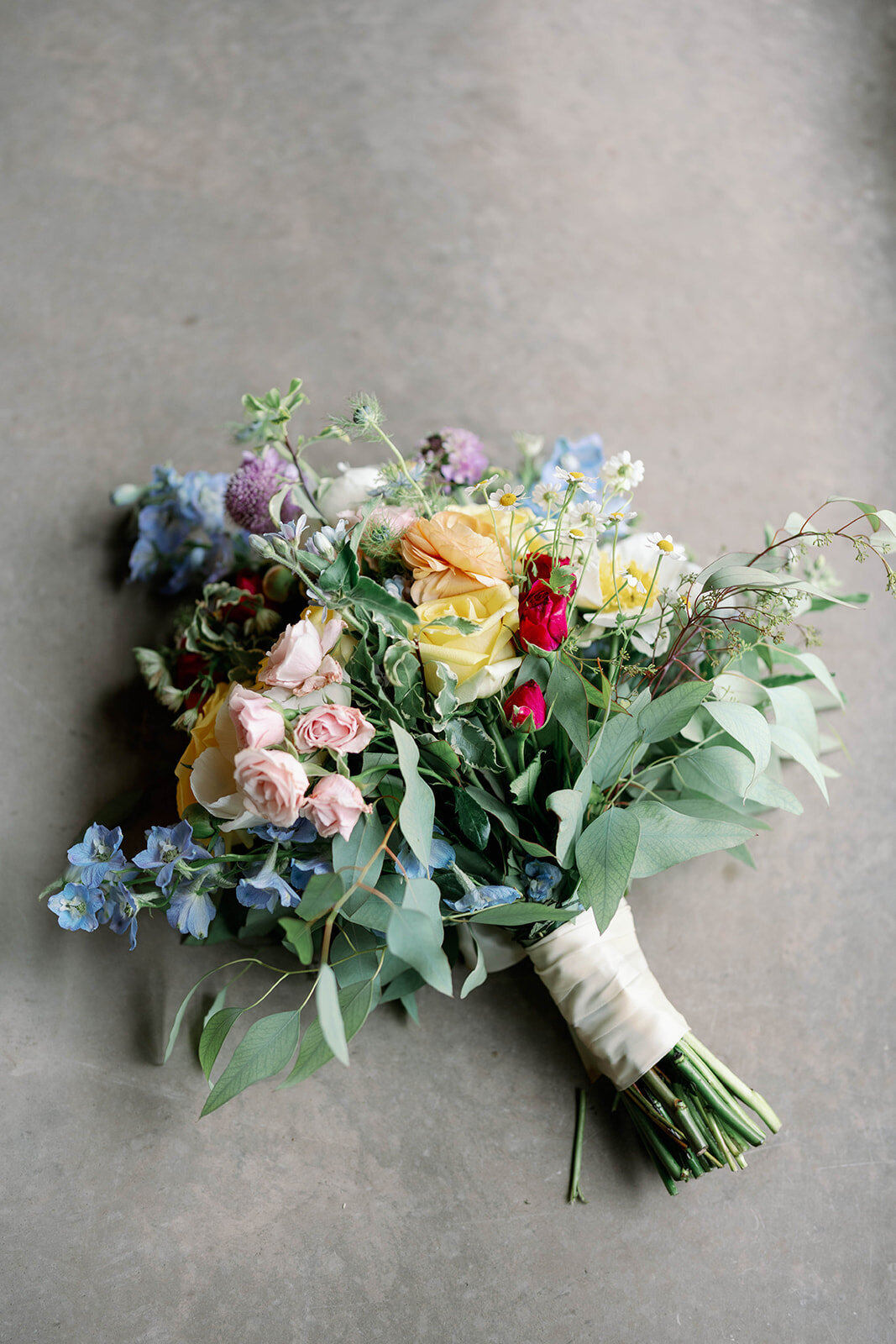 Close-up of the bride’s white and green bouquet resting on concrete flooring at The Blue Heron Barn in Kalamazoo, MI.