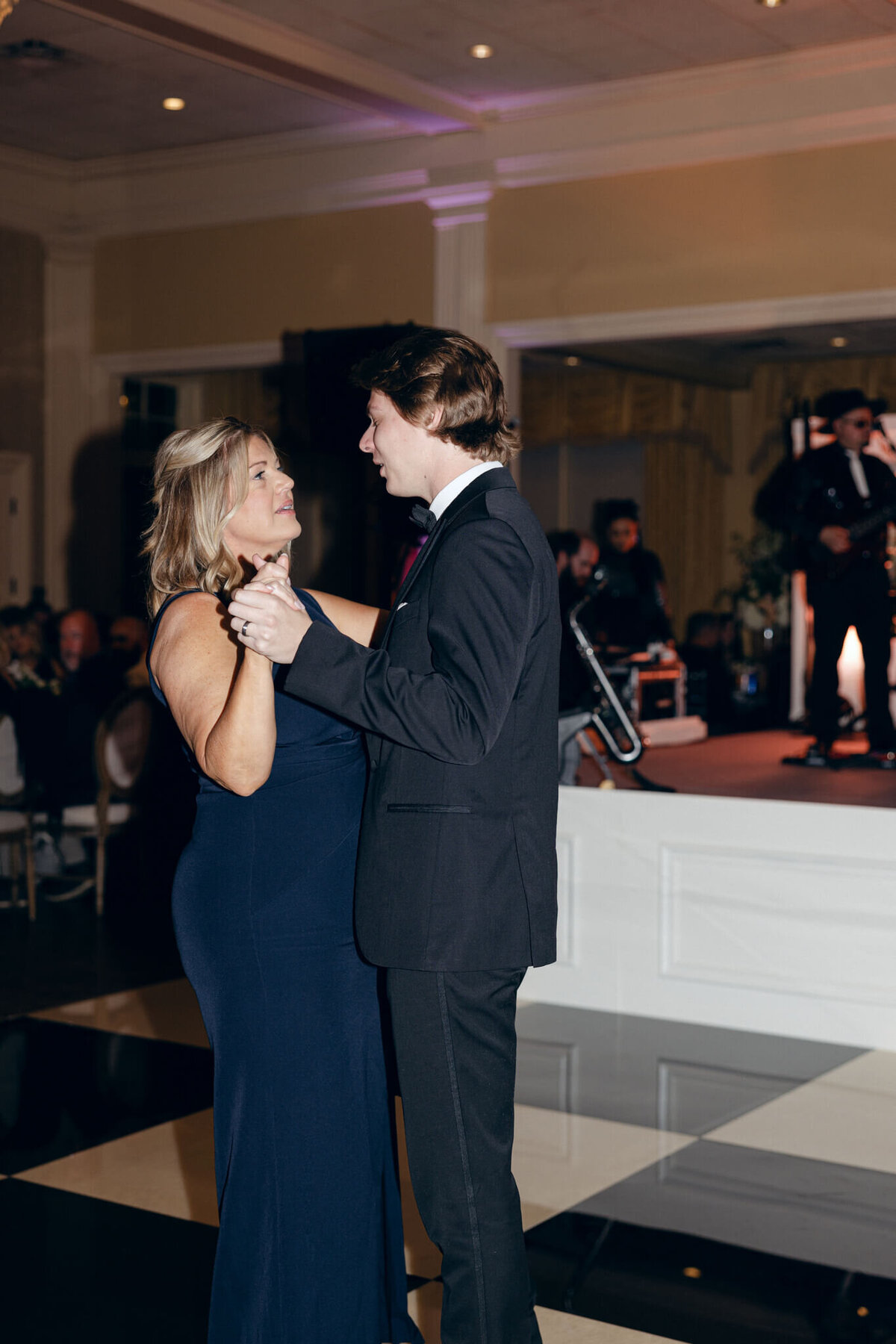 A wedding photo of the groom dancing with his mom at the reception