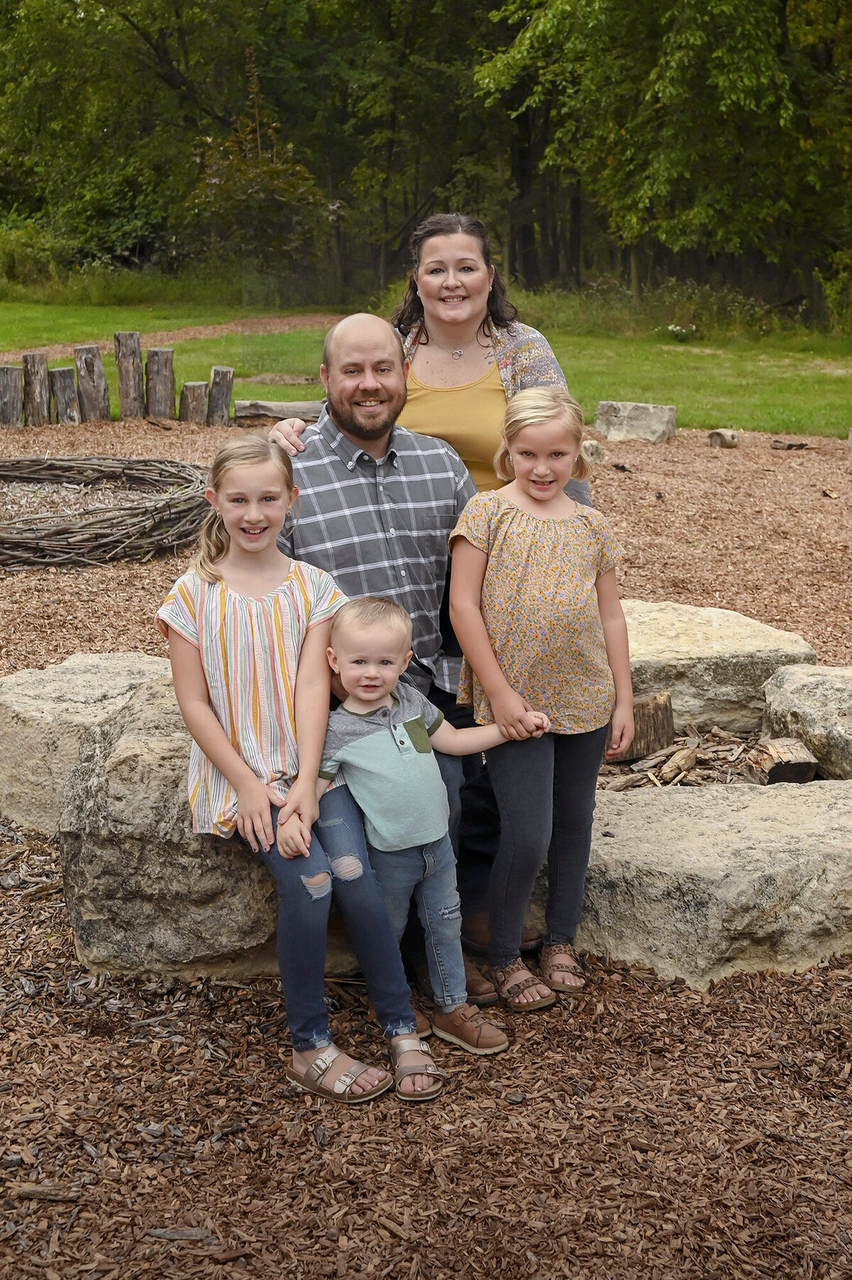 A family of 5 posing on rocks in a natural outdoor setting with greenery around them