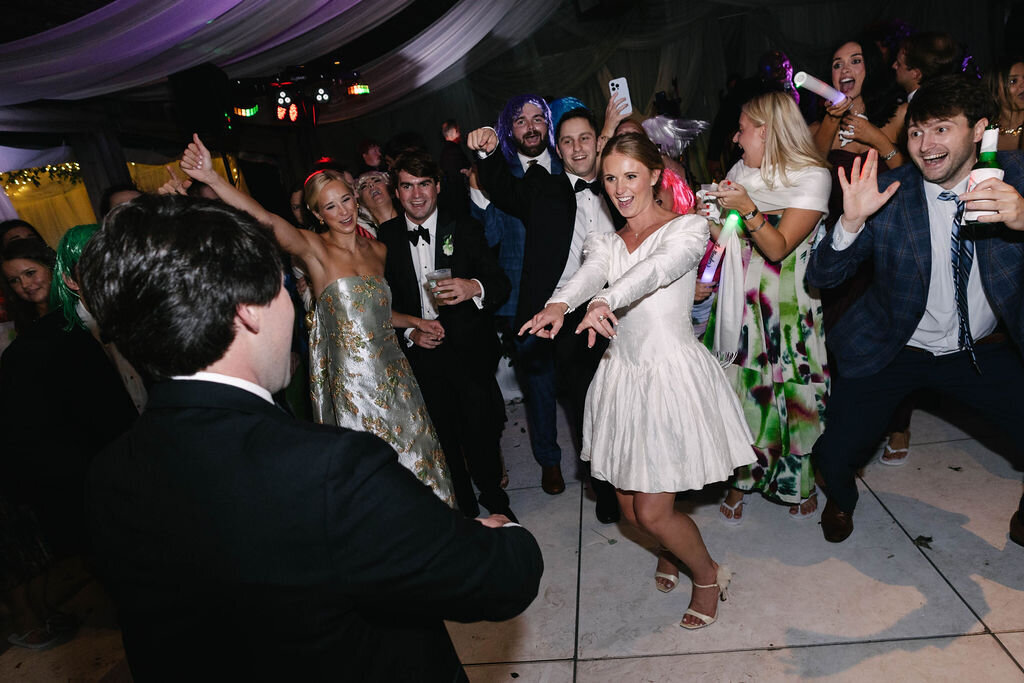 Bride and guests wearing colorful wigs dance enthusiastically during the wedding reception at The Bascom in Highlands, North Carolina.