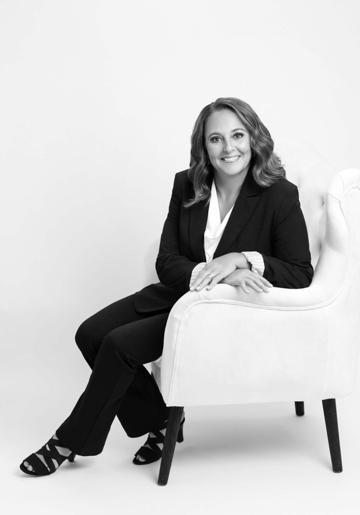 Black-and-white portrait of a professional woman seated in a white chair.