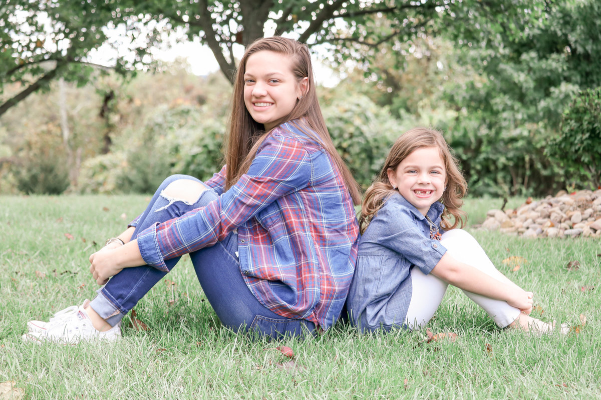 Sisters sitting back to back on the grass