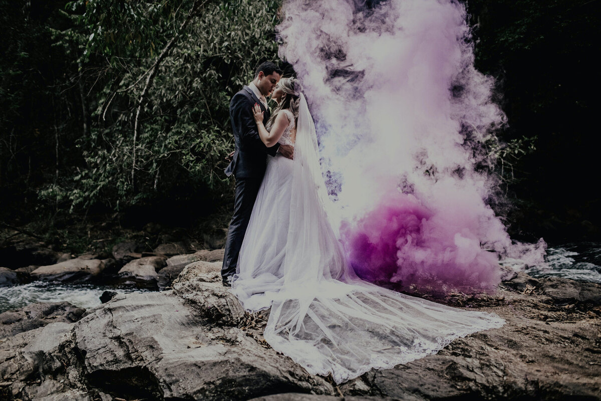 Bride and groom kissing each other on the lake and has purple smoke