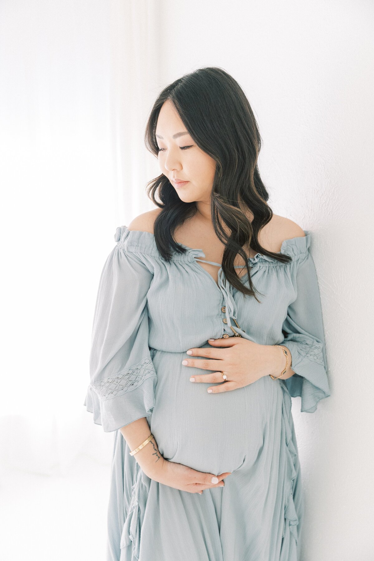 Beautiful asian mom wearing blue free people dress looking over shoulder while holding on to baby bump