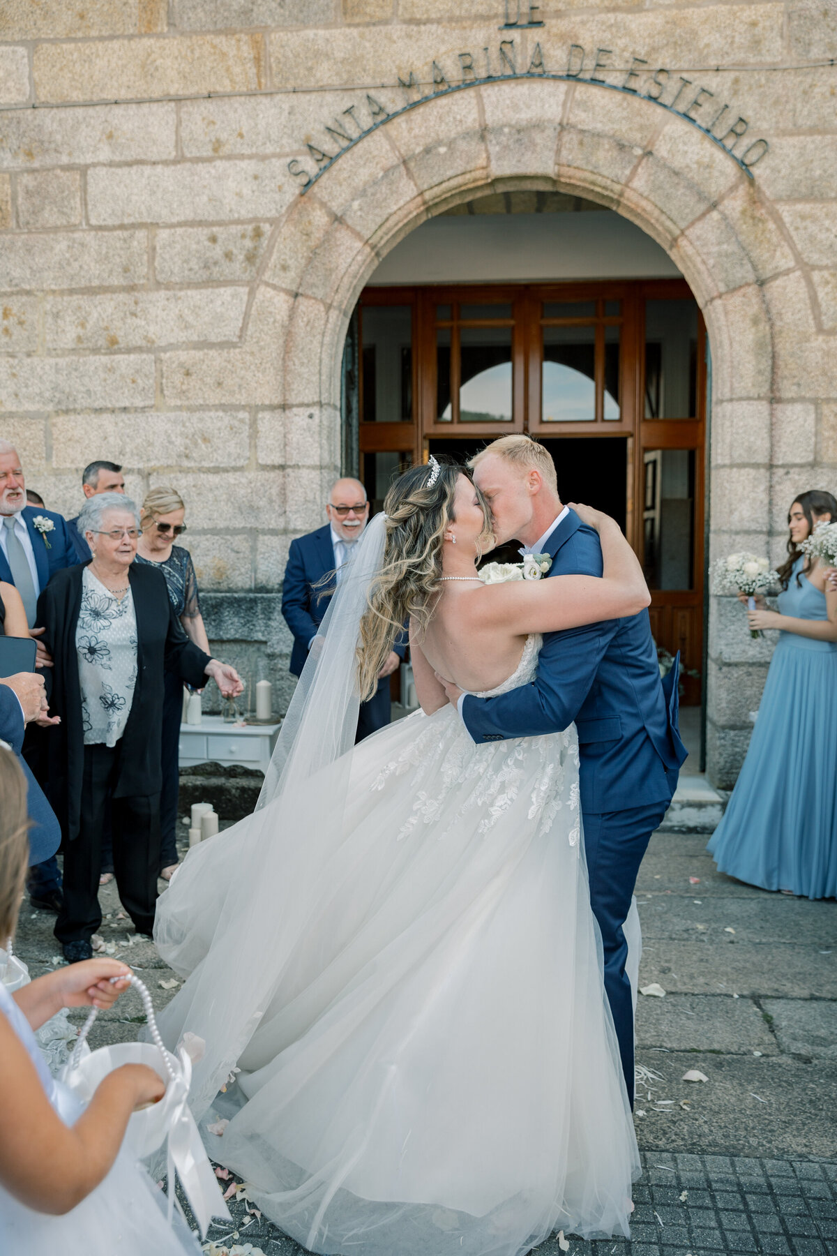 Church Wedding In Spain | A bride and groom kiss surrounded by family and friends as they exit the church where their wedding ceremony was held.