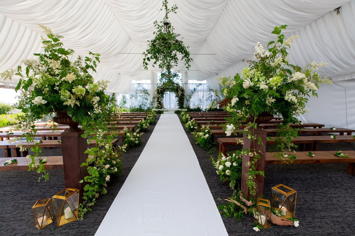 Wedding ceremony decorated with greenery along the aisle, a large wedding arbor, greenery in chandeliers in Newcastle tent