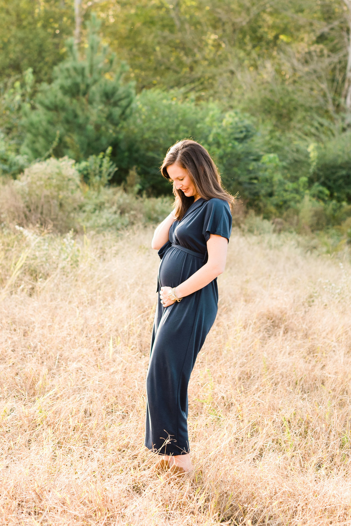 Mom wearing a blue gown holds her belly and smiles during a maternity photography session in Raleigh. Photographed by Raleigh NC Family Photographer A.J. Dunlap Photography.