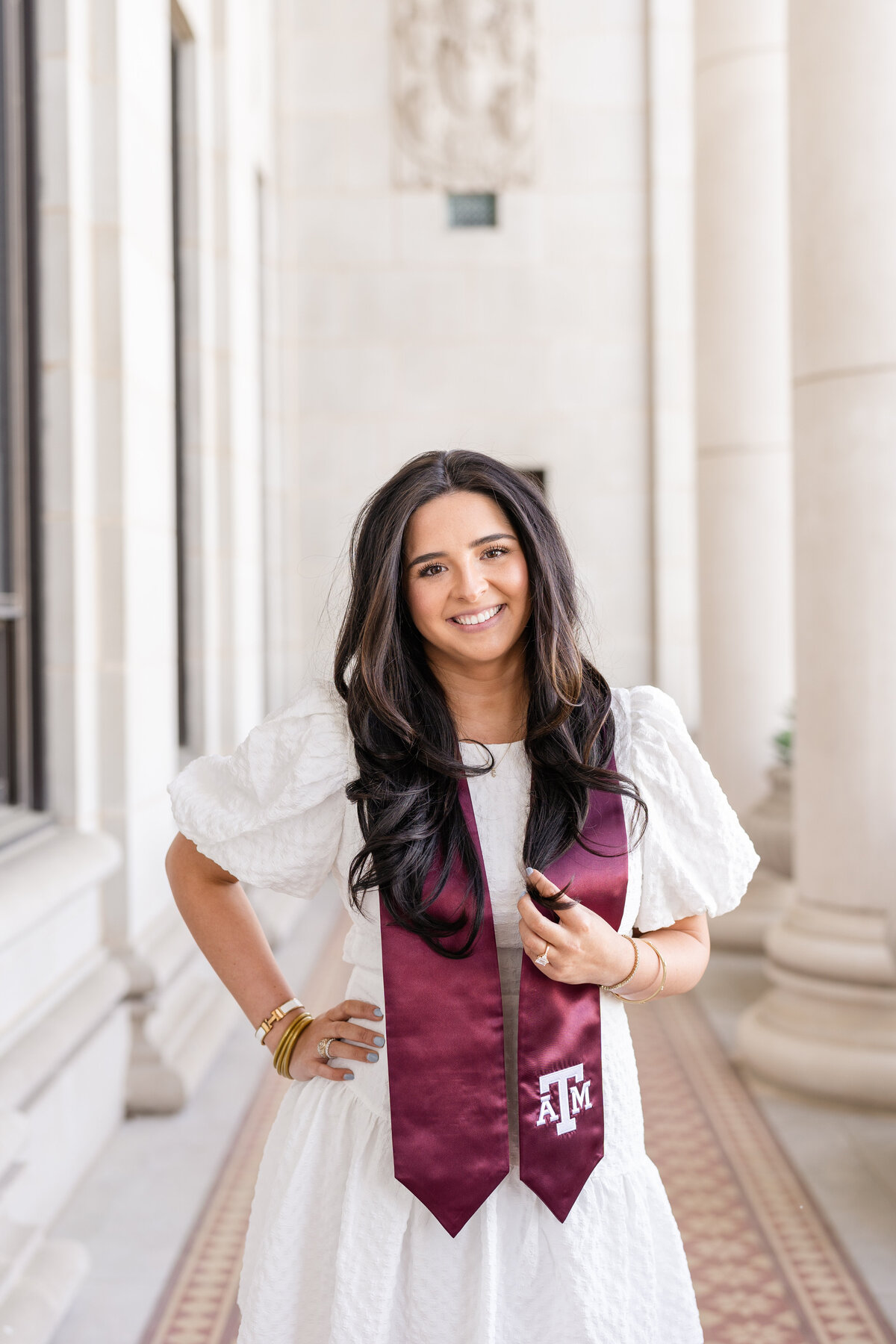 Texas A&M senior girl holding Aggie stole and smiling with hand on hip and wearing white dress in columns of the Administration Building